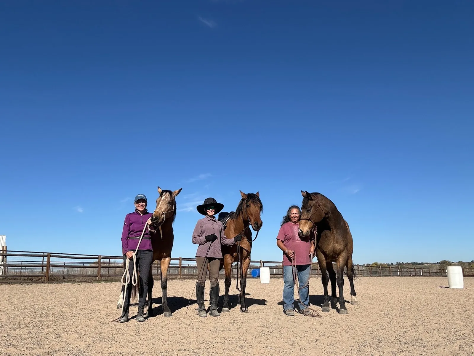 Three boarders standing with their horses in the arena under a blue Colorado sky